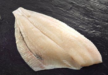 Raw, pale white sole fillet on a dark, textured surface.