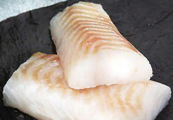 Two white and tan cod fillets on a dark surface.