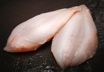 Two raw fish fillets on a dark surface, pale pinkish-white flesh.