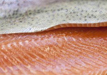 Close-up of raw salmon fillet, showing pink flesh and silver skin with tiny dark spots.