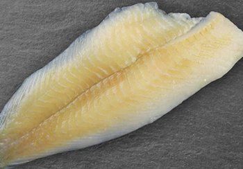Raw fish fillet, pale yellow and white, on a dark gray surface.