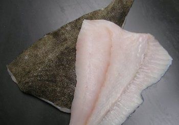 Halibut fillet, white flesh, next to dark, rough skin, on a dark surface.