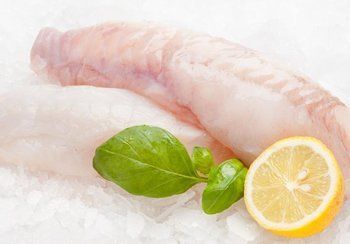 Raw fish fillets with basil and lemon half on ice.