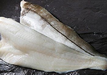 Two raw, white fish fillets on a dark surface.