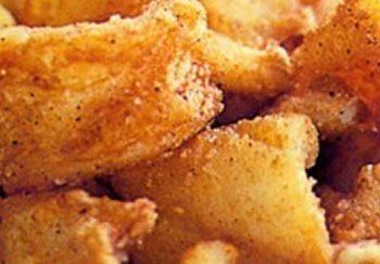 Close-up of seasoned, golden-brown fried potato wedges, some dusted with seasoning.
