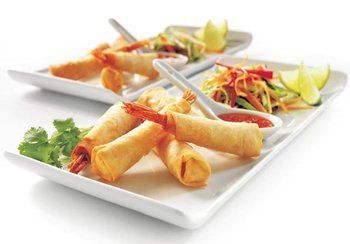 Fried shrimp spring rolls with sauce, salad, and lime wedges on white plates.