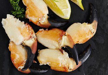 Cooked stone crab claws with lemon slices and parsley on a dark surface.