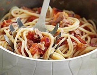 Spaghetti with red tomato sauce and meat in a metal pot, being lifted by a serving fork.