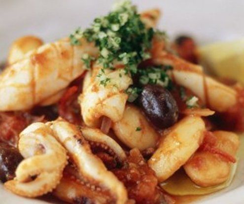 Cooked squid with tomatoes, olives, and herbs on a white plate.