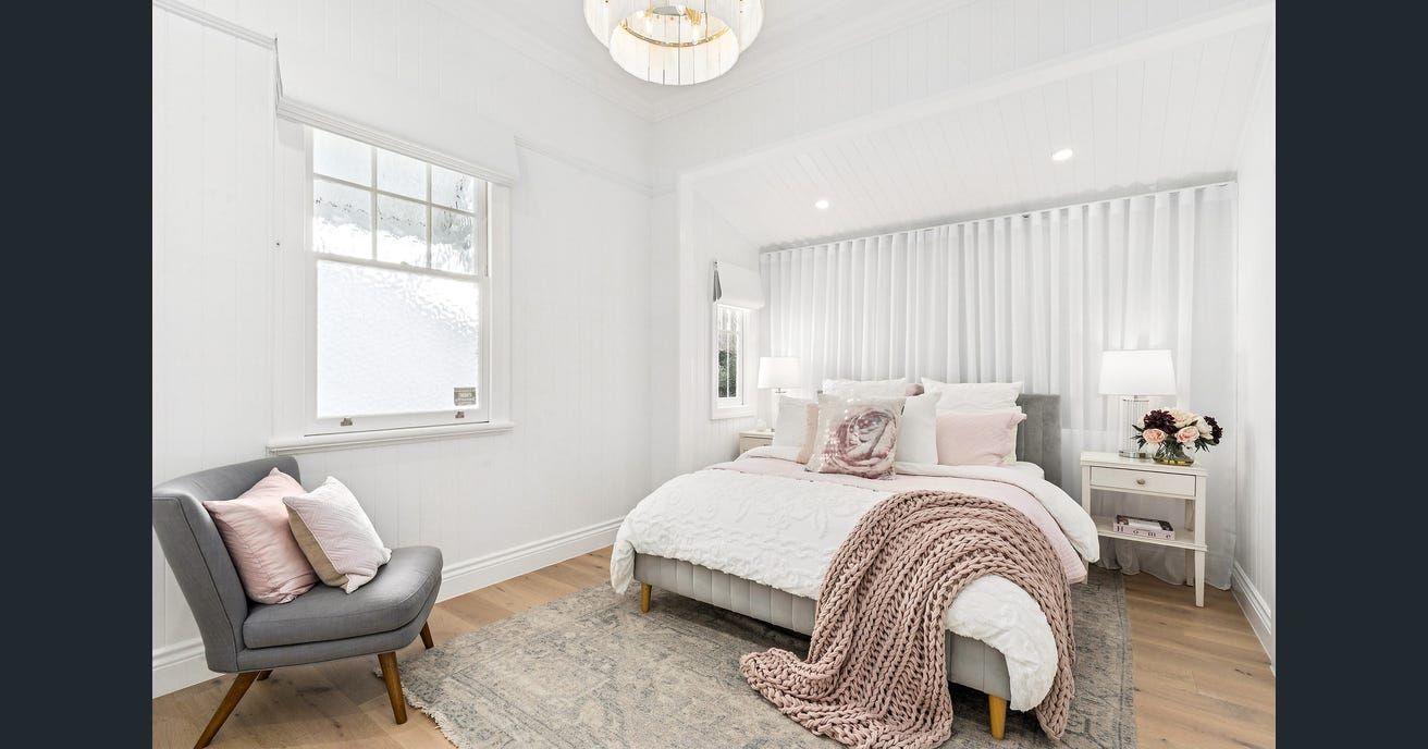 Bedroom with gray chair, bed with pink accents, sheer curtains, and light wood flooring. — Caprice Cabinets in Coolum Beach, QLD
