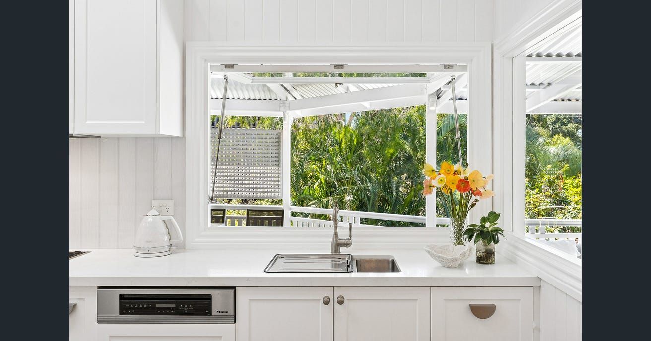 Bright white kitchen with a window looking out onto greenery; flowers on the countertop. — Caprice Cabinets in Coolum Beach, QLD