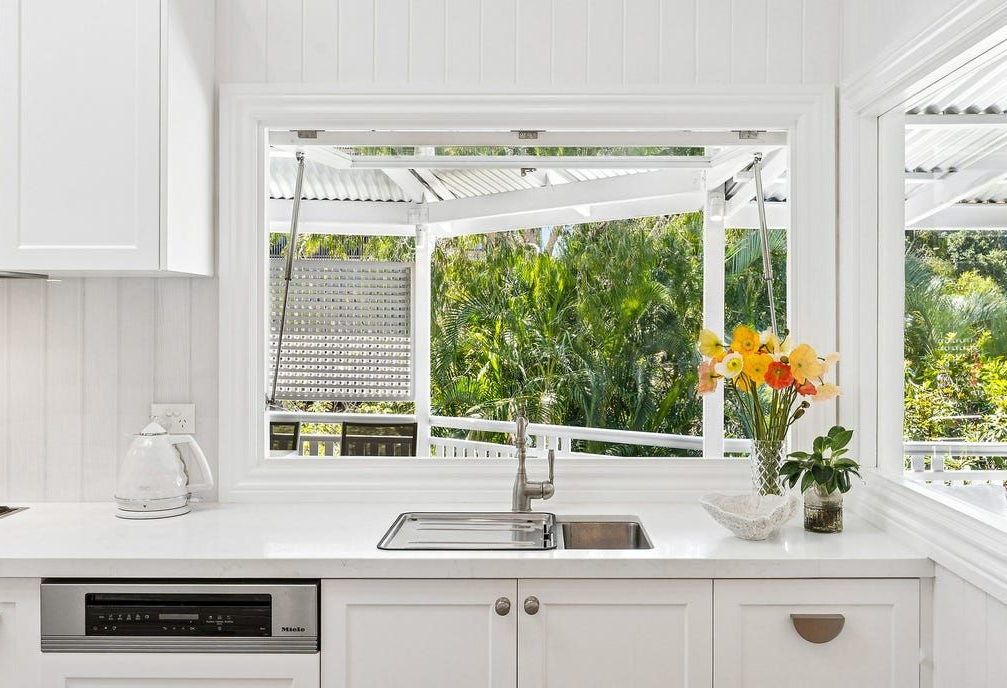 Bright white kitchen with open window overlooking lush greenery and a sink — Caprice Cabinets in Coolum Beach, QLD