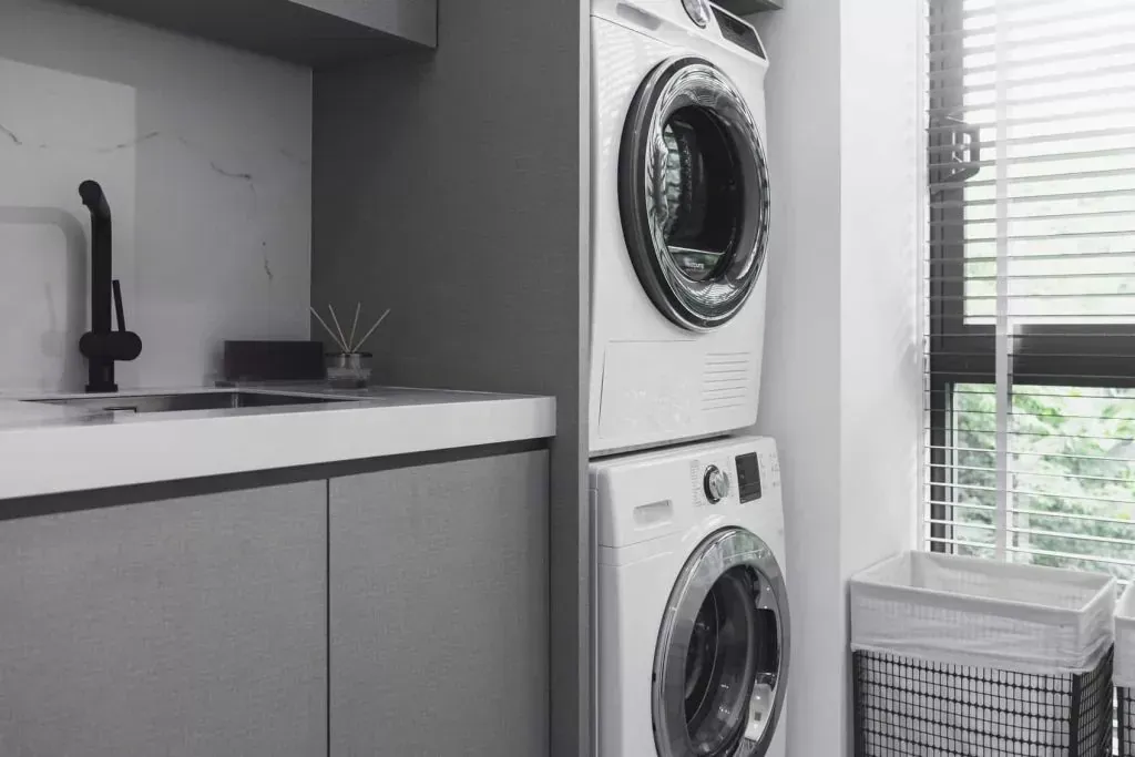 Stacked washer and dryer in a laundry room with a sink and a window. — Caprice Cabinets in Coolum Beach, QLD