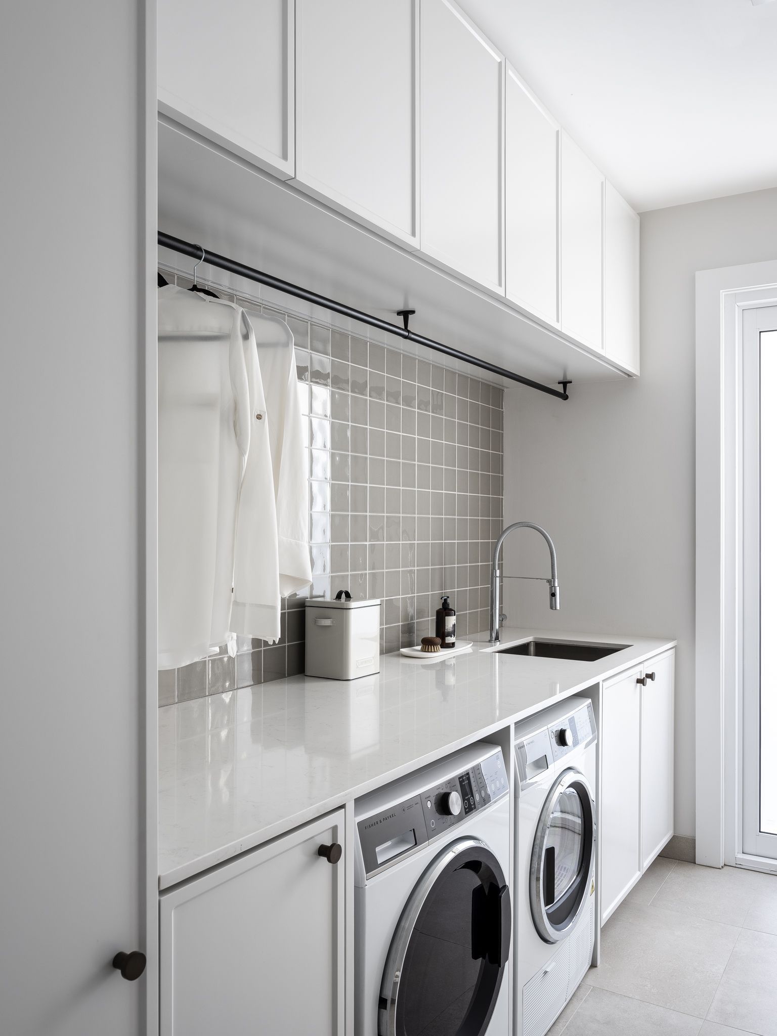 Modern laundry room with white cabinets, gray backsplash, washer, dryer, and drying rod. — Caprice Cabinets in Coolum Beach, QLD