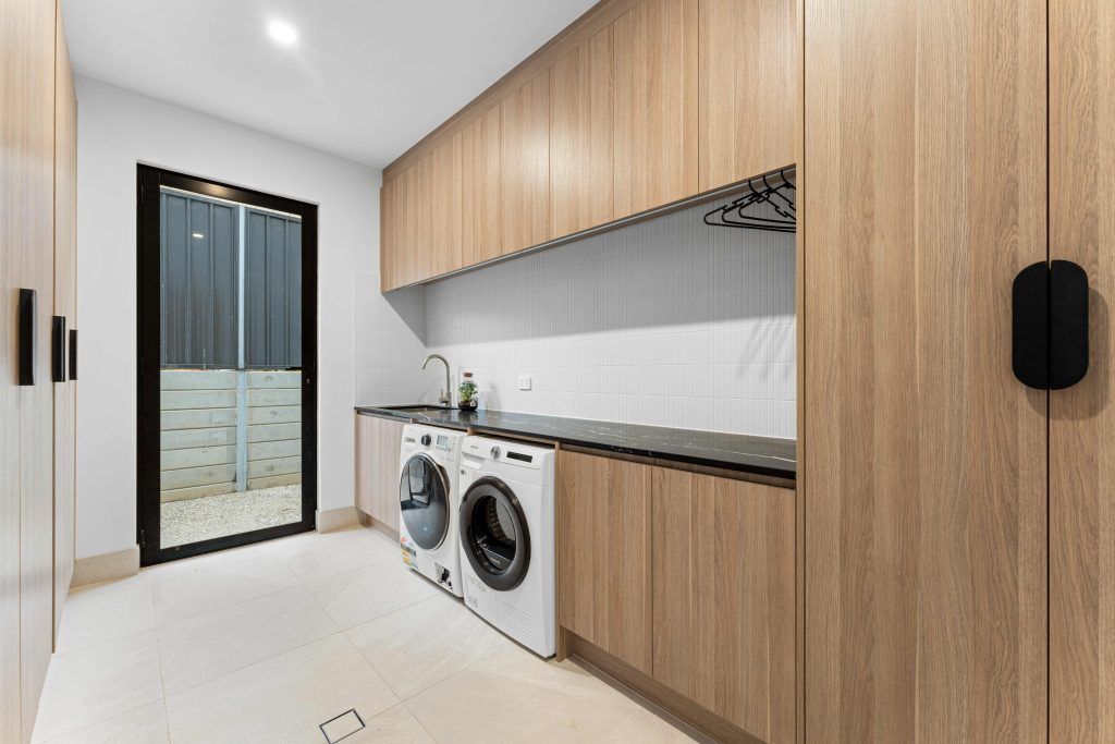 Laundry room with light wood cabinets, white appliances, and a black-framed glass door. — Caprice Cabinets in Coolum Beach, QLD