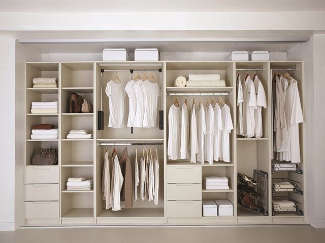 Closet with light-colored shelving, drawers, and hanging rods filled with folded and hanging white clothing and accessories.