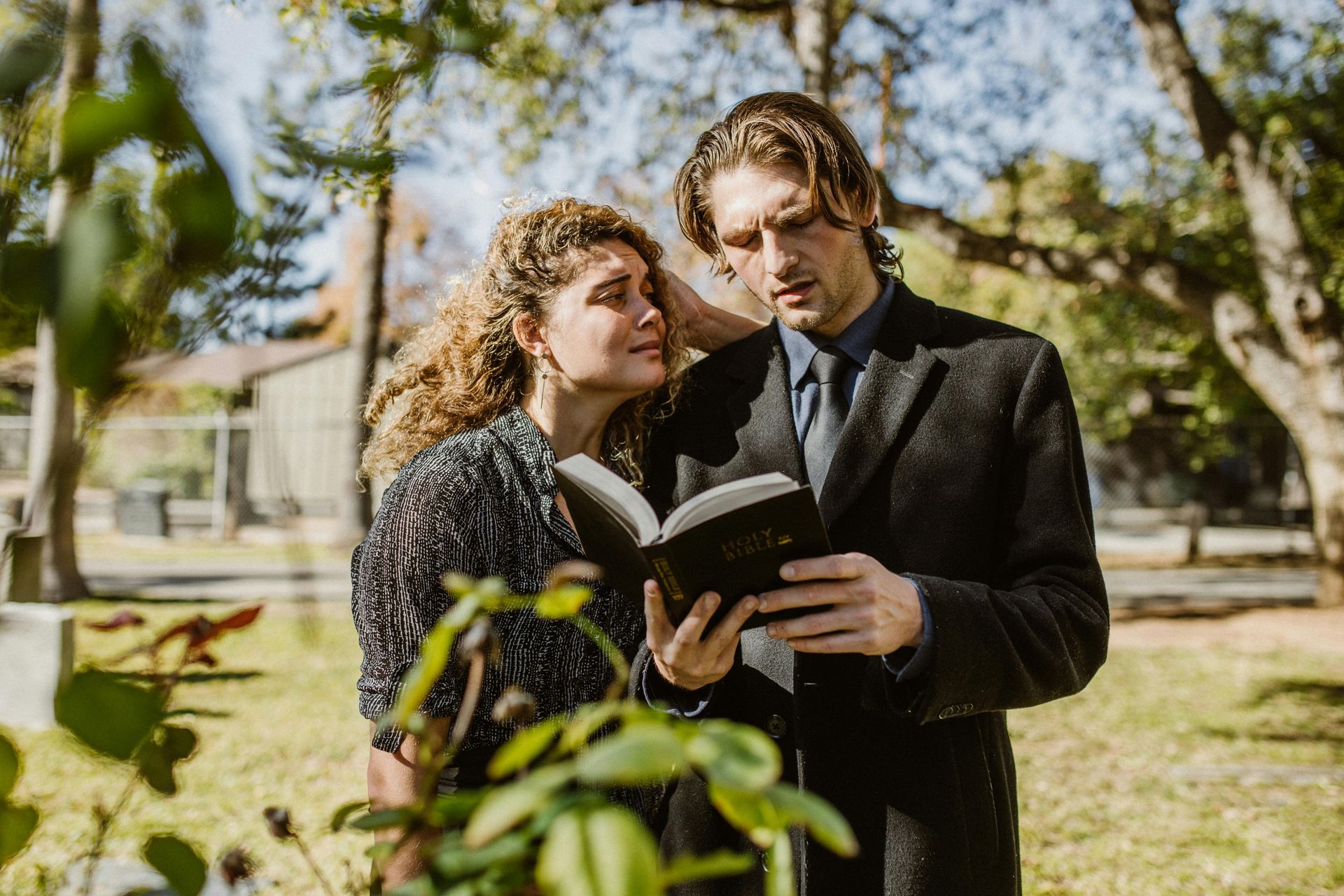 A man and a woman are reading a bible together in a park.