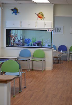 A waiting room at Riverside Pediatrics with tables and chairs and an aquarium on the wall.