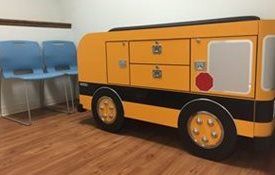 A yellow school bus is sitting in a waiting room next to blue chairs at Riverside Pediatrics.