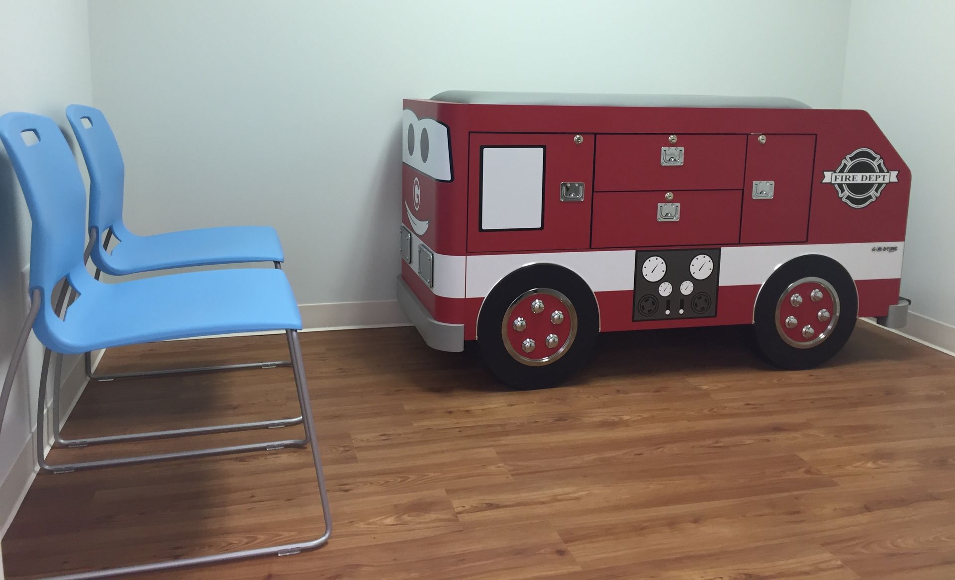 A pediatrician's exam room with two chairs and an exam table that looks like a fire truck at Riverside Pediatrics.