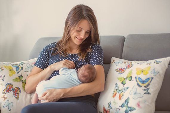 A woman is breastfeeding her baby while sitting on a couch.