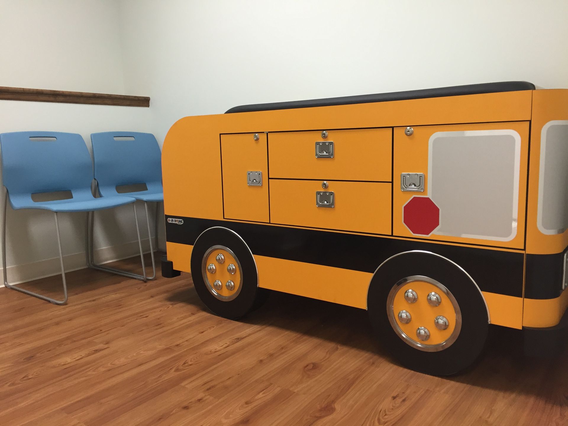 A pediatrician's exam table with two chairs and a dresser in the shape of a school bus at Riverside Pediatrics.