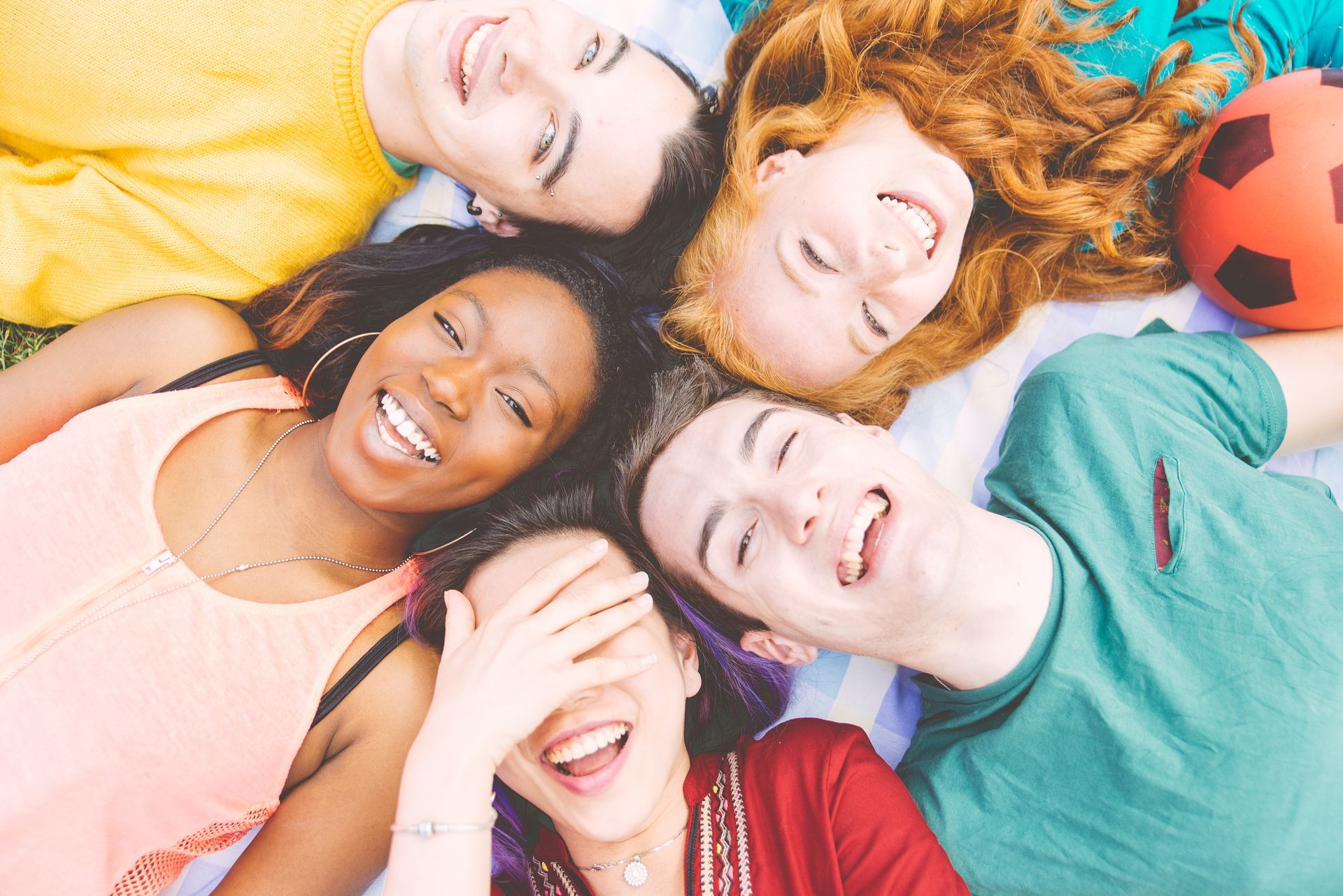 A group of young people are laying in a circle on the ground.