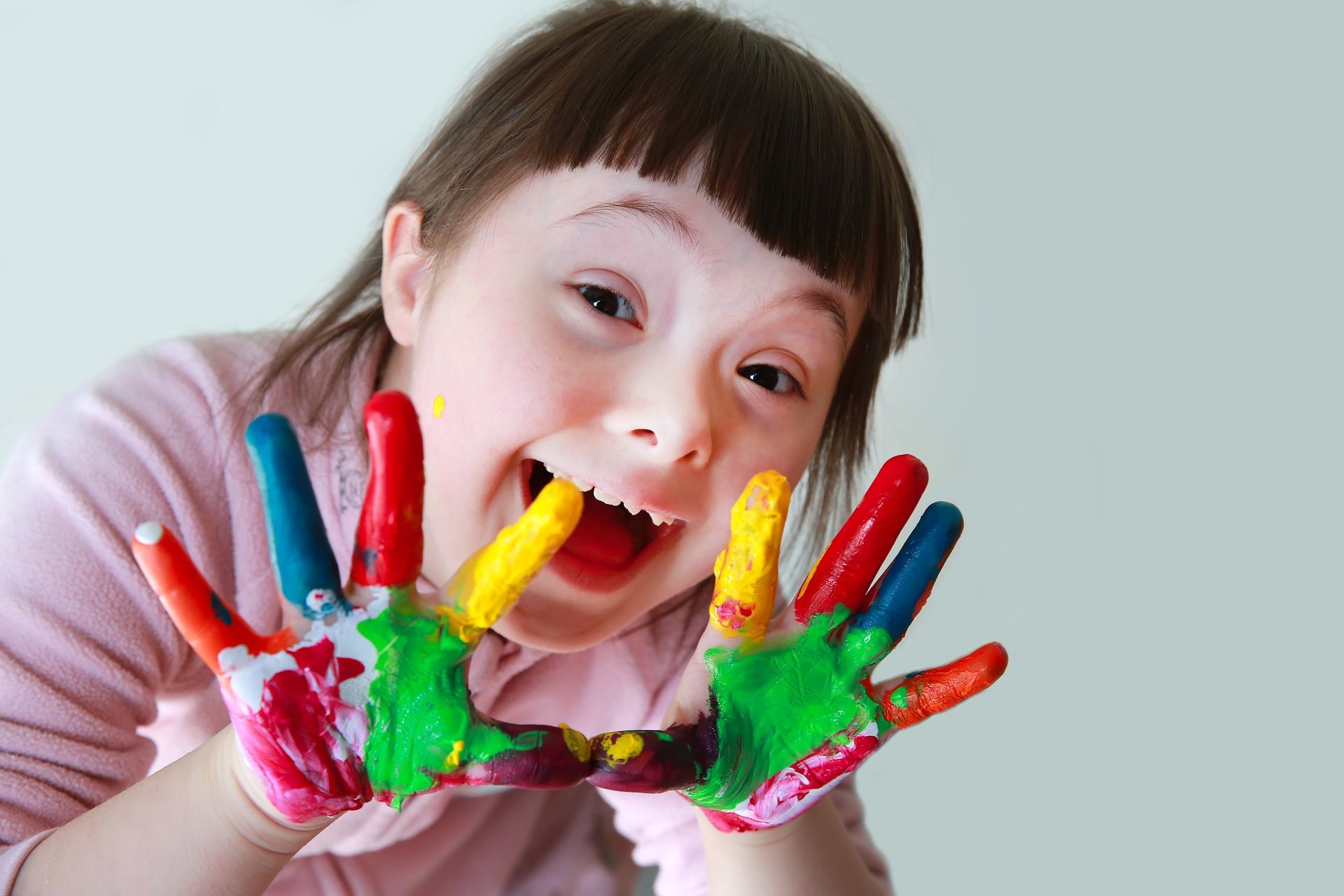 A young girl with down syndrome is holding her hands painted in different colors.