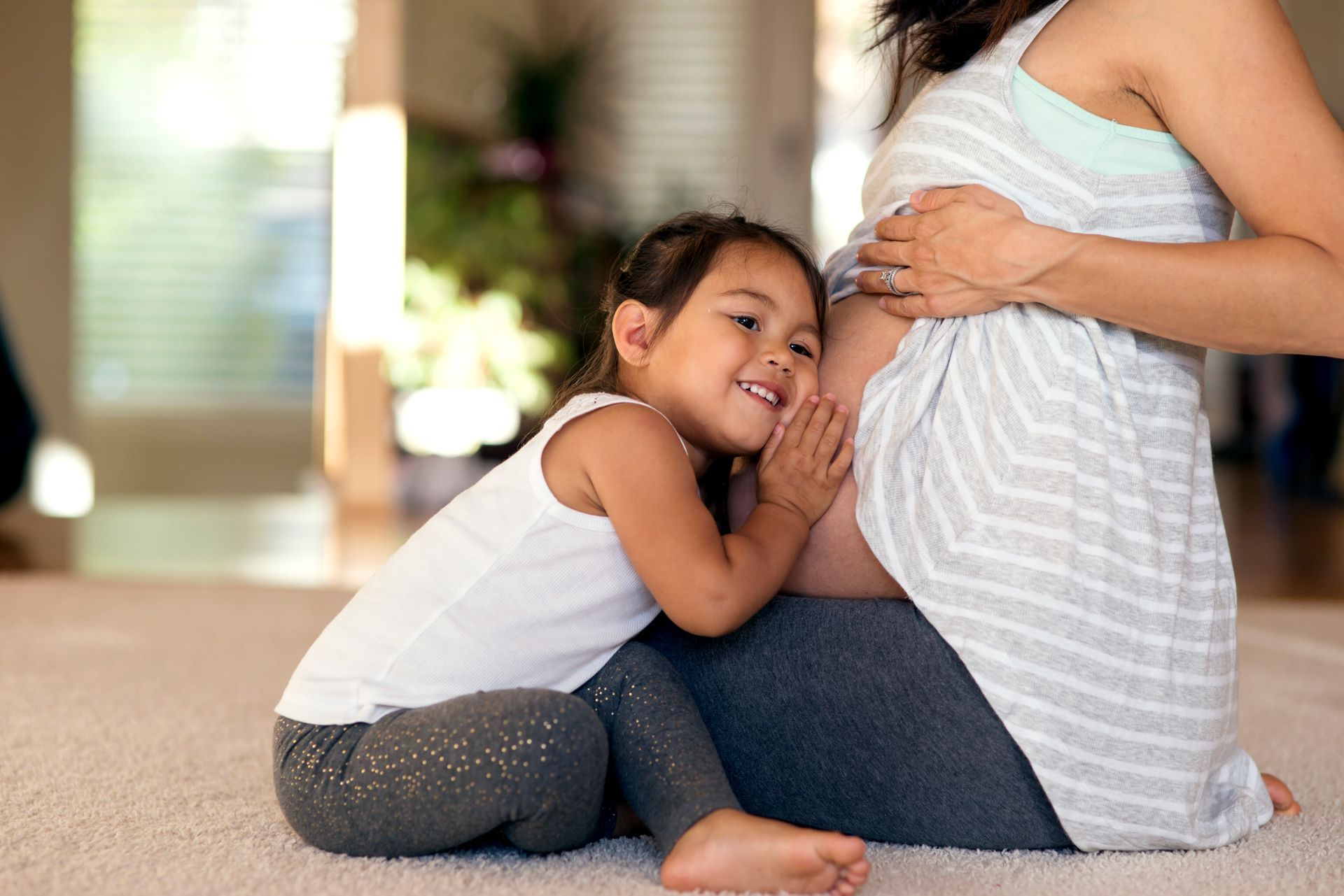 A little girl is hugging a pregnant woman 's belly.