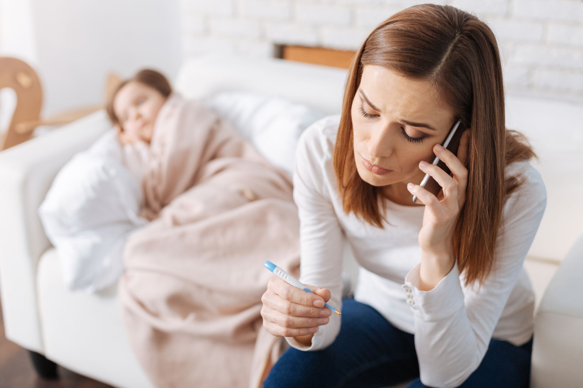 A woman is holding a thermometer while talking on a cell phone.