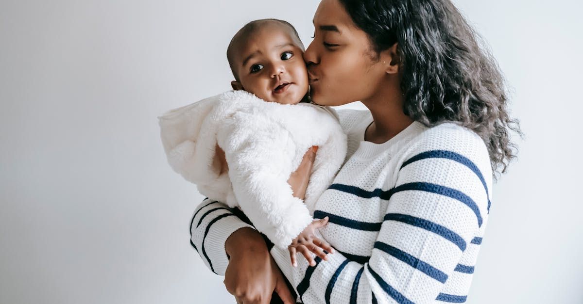 A woman is holding a baby in her arms and kissing it on the cheek.