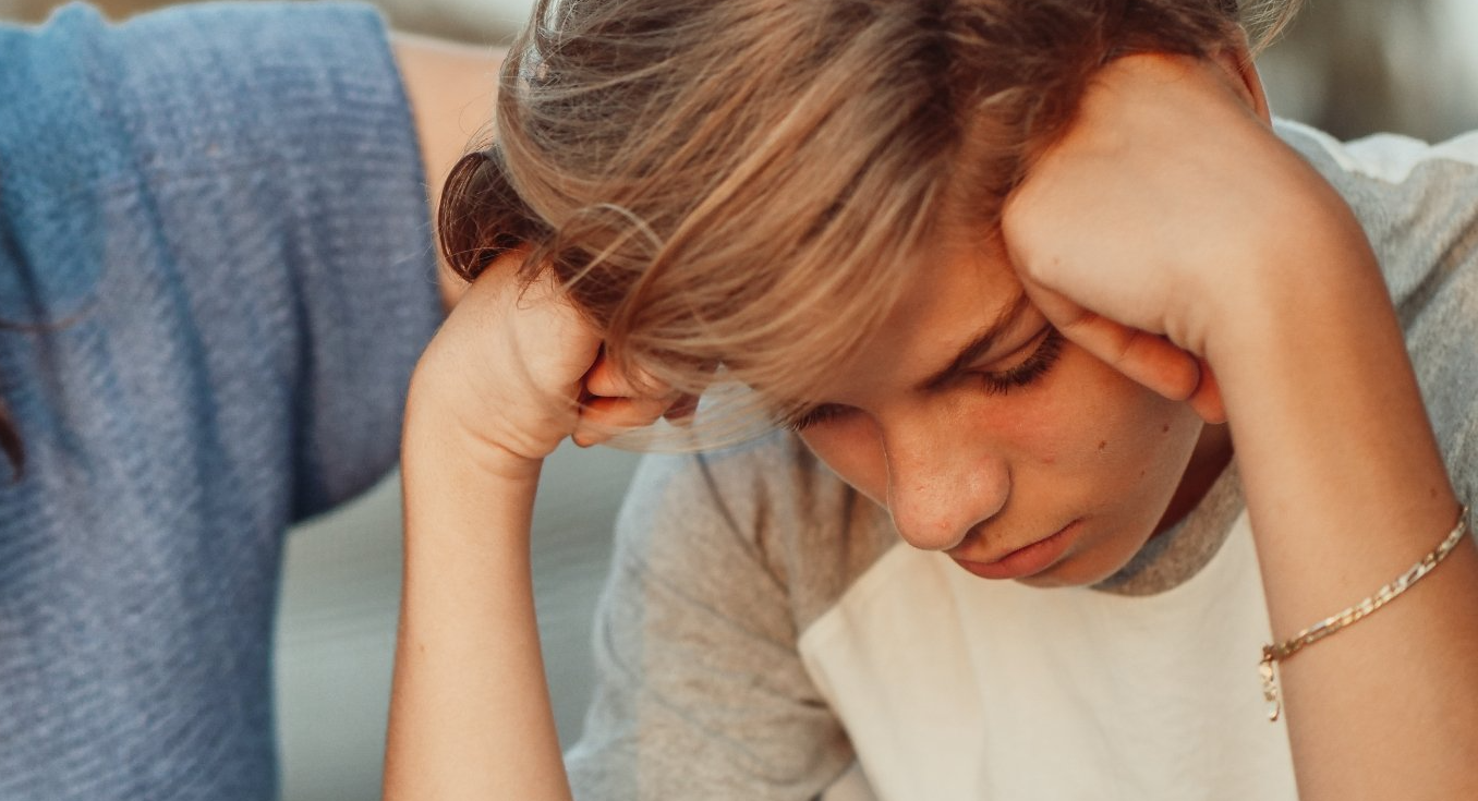 A young boy is sitting down with his head in his hands.