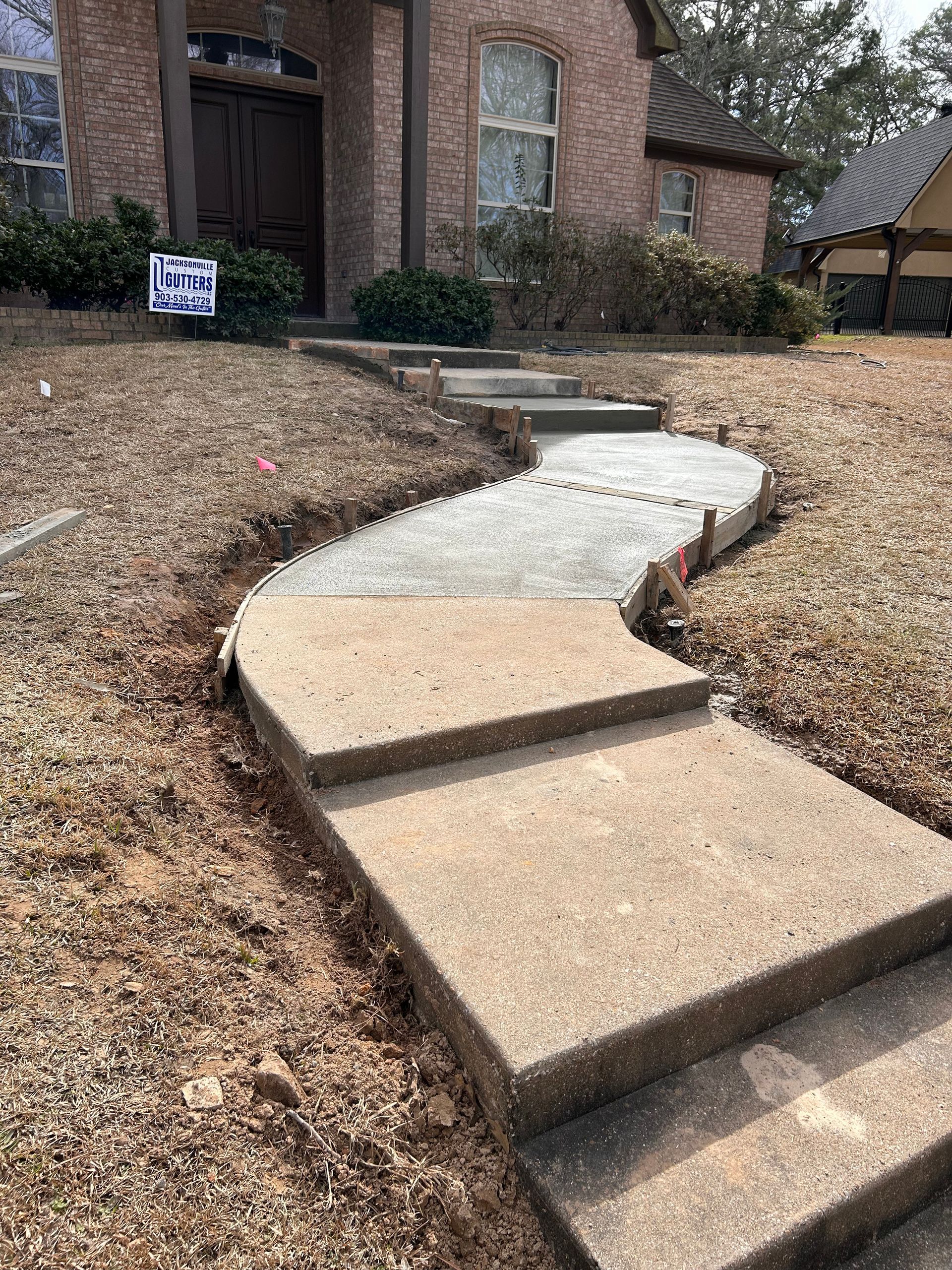 A concrete walkway is being built in front of a brick house.