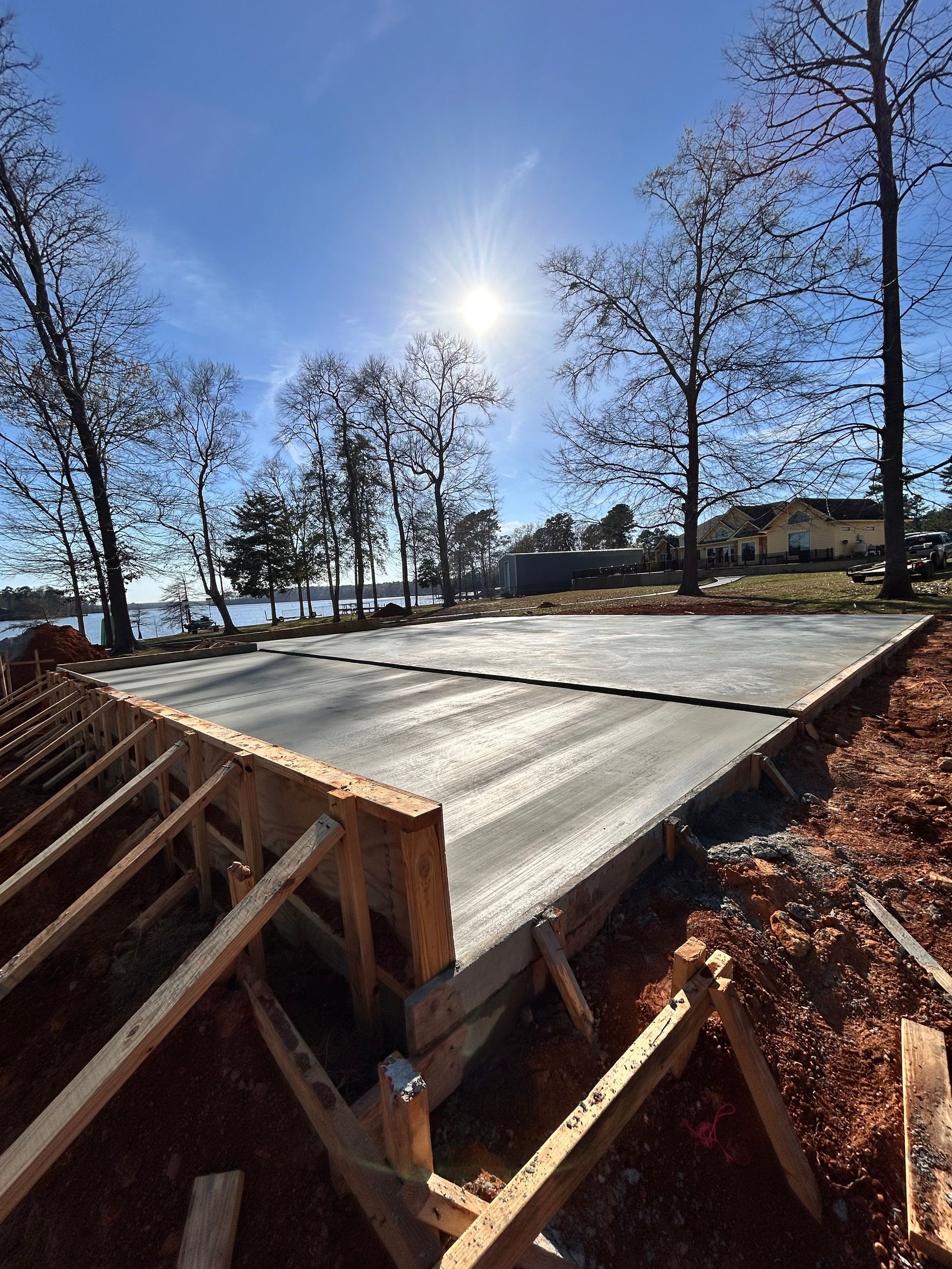 A freshly poured concrete slab foundation under construction, framed with wooden boards, outdoors on a sunny day.