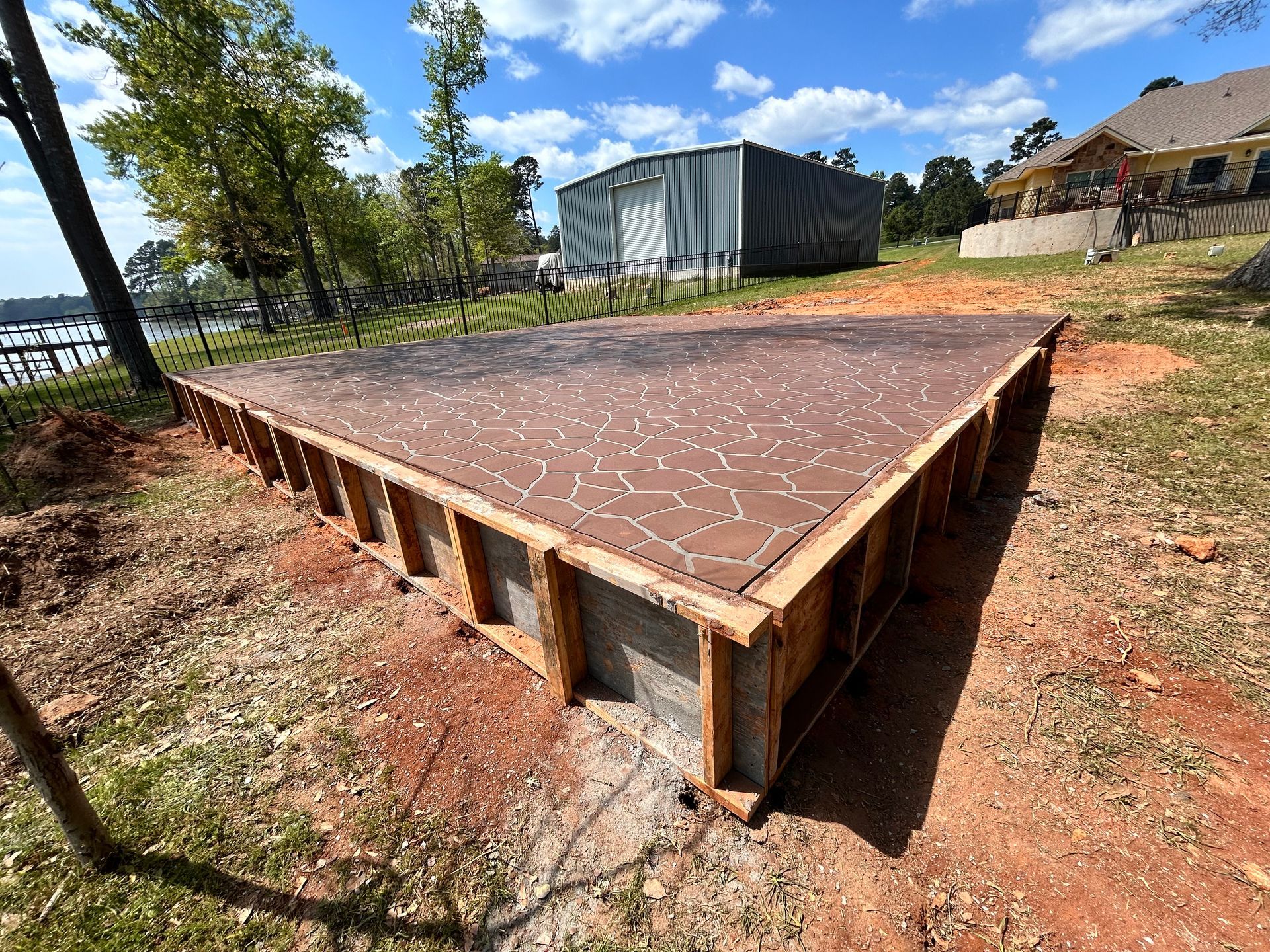 A wooden form for a concrete foundation sits on red dirt, with a metal building and blue sky in the background.