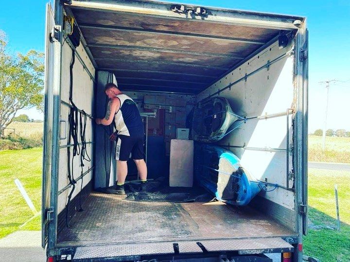 A Man Is Standing In The Back Of A Moving Truck — Easy Flow Removals In South West Rocks, NSW