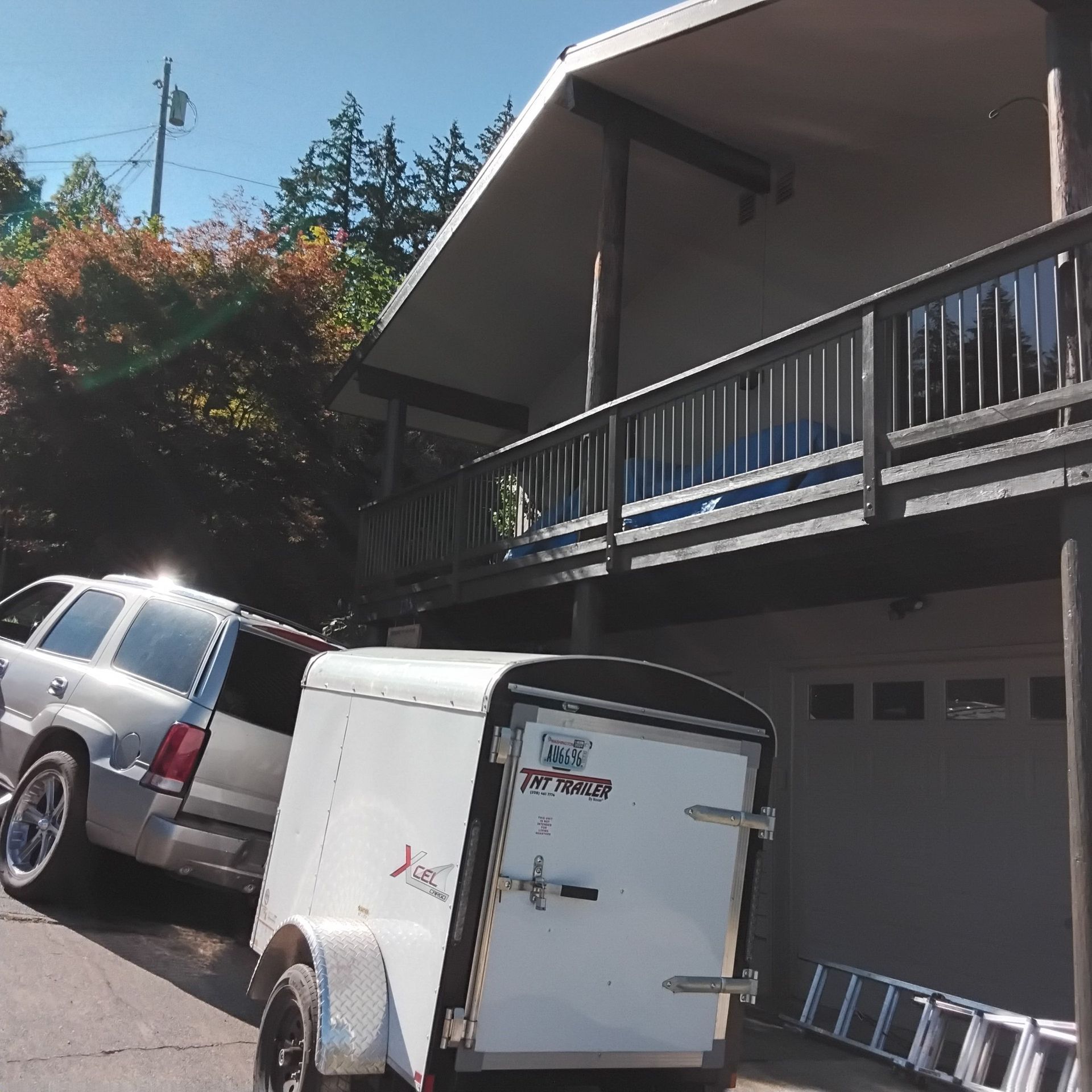 SUV backing up to a white cargo trailer in front of a house with a balcony. Ladder next to the garage.