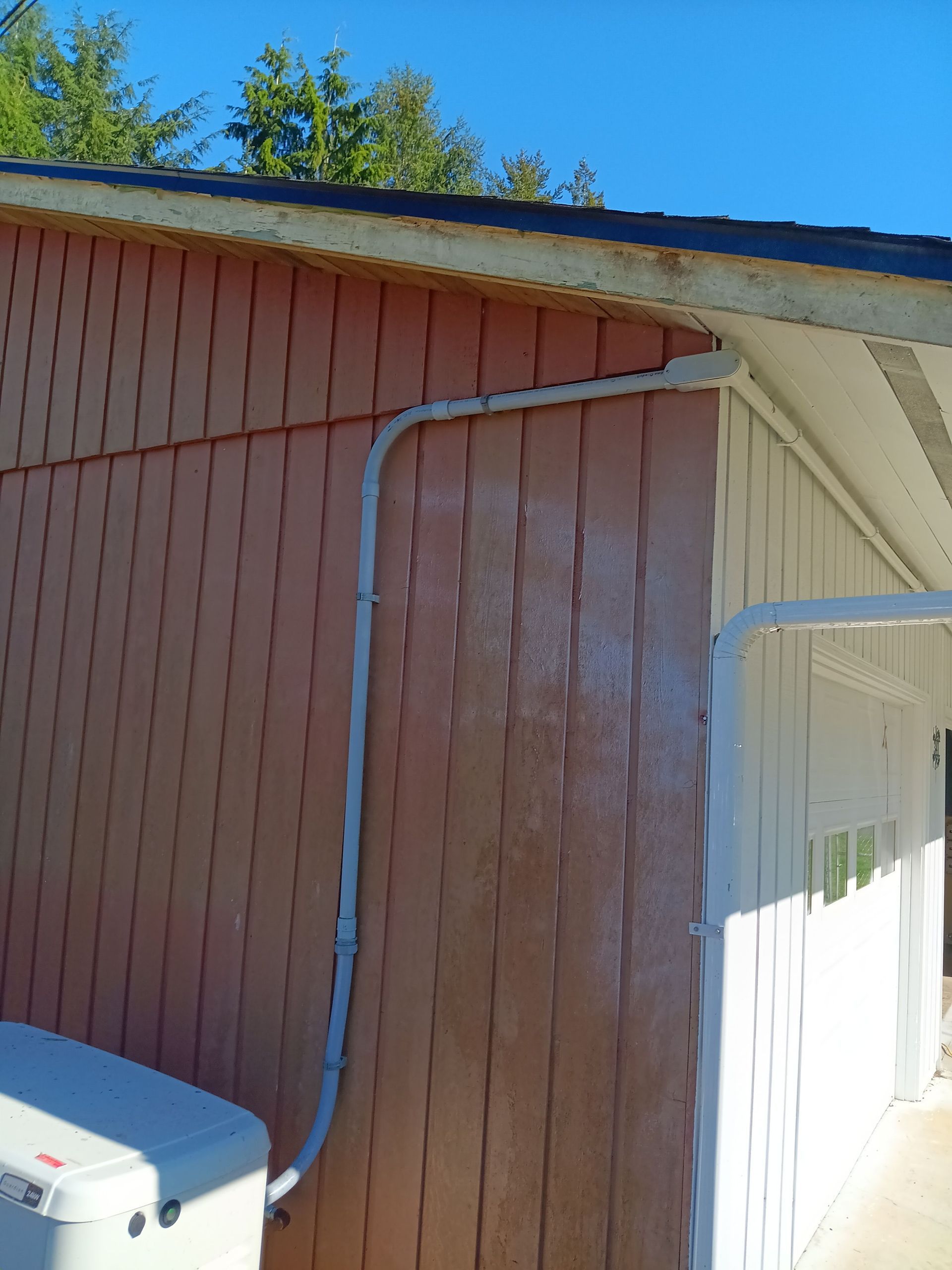 A white electrical conduit runs up the pinkish-brown siding of a building near a white porch overhang.