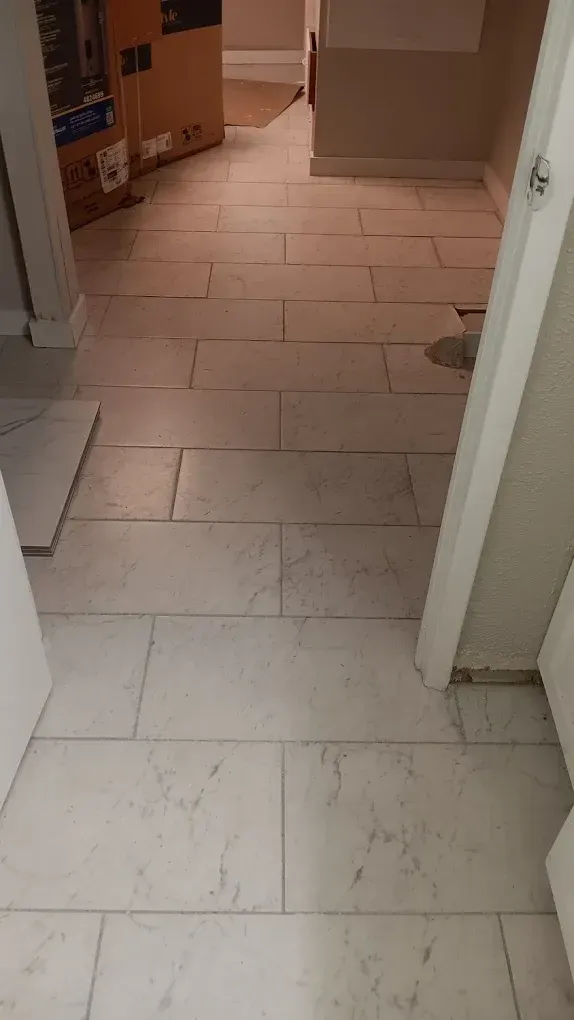 White rectangular floor tiles in a hallway, partially installed. Doors, boxes visible.