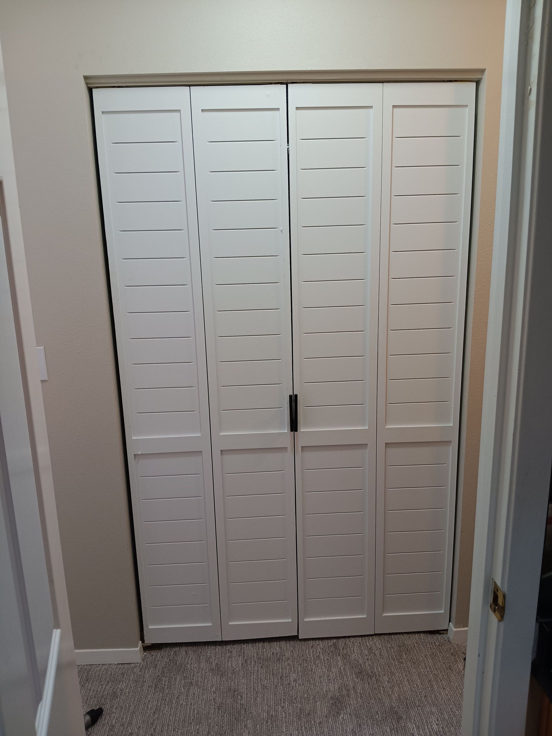 White folding closet doors with horizontal slats in a beige hallway, closed.