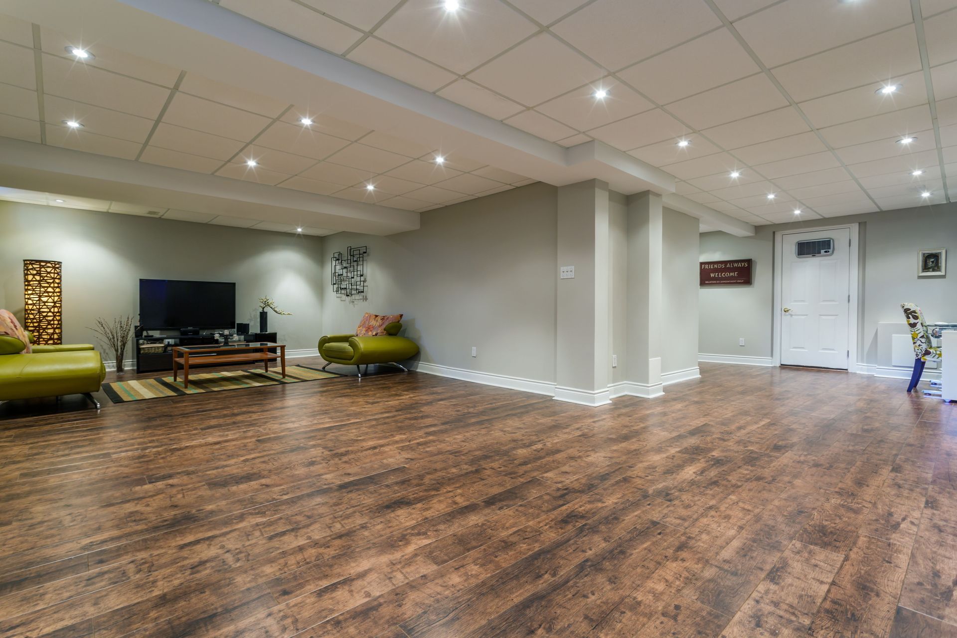 Spacious finished basement with dark wood-look flooring, light gray walls, and recessed lighting. Contains seating and a TV.