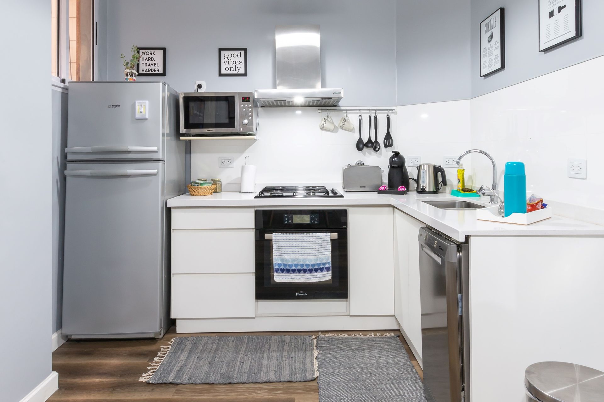 A small, modern kitchen with white cabinets, silver appliances, and a gray rug.
