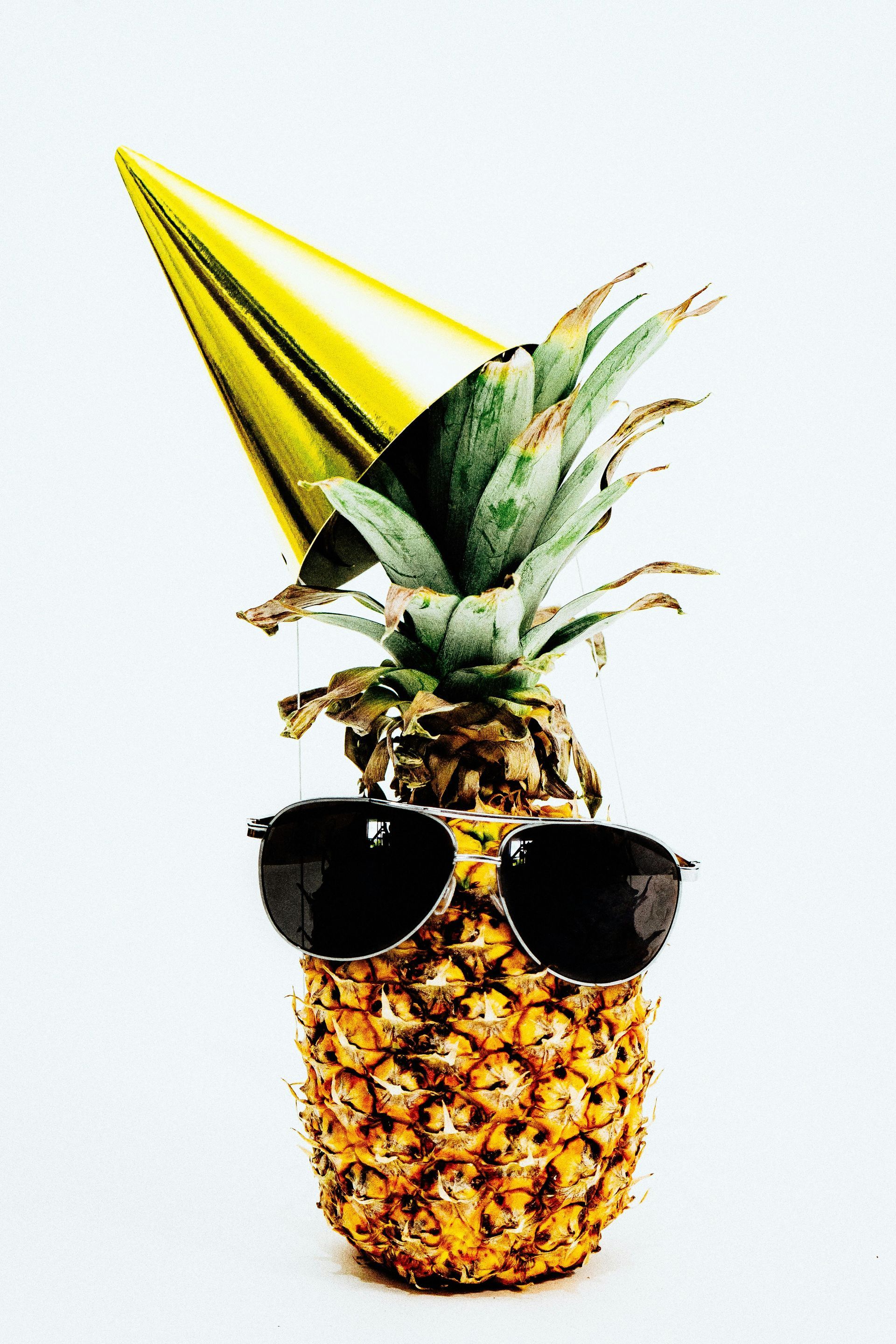A pineapple wearing a party hat and sunglasses