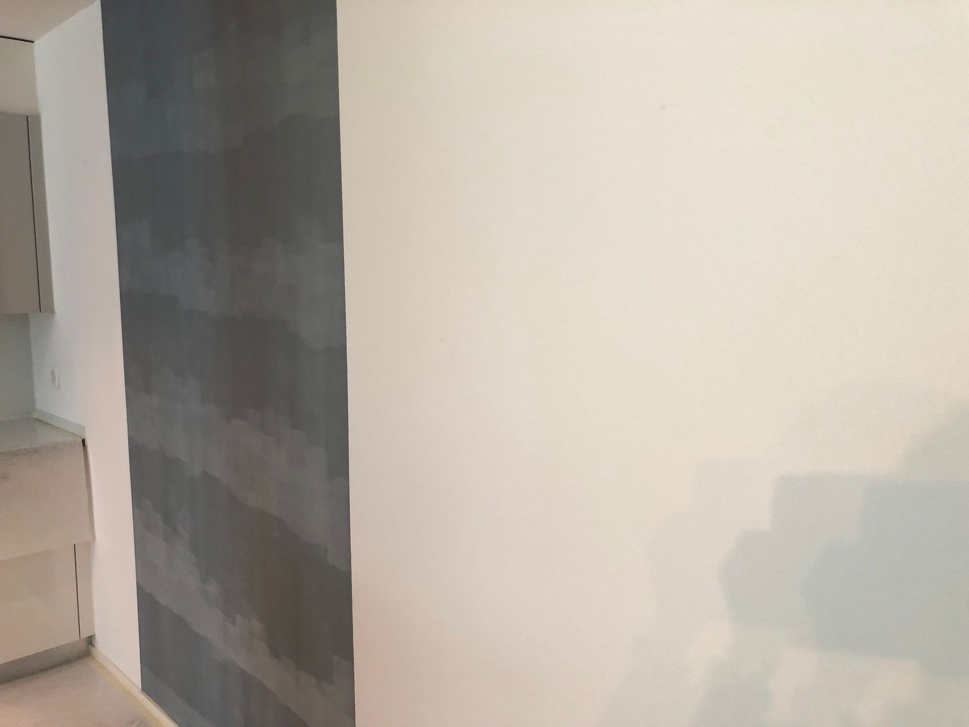 In einer Küche wird eine weisse Wand mit einem grauen Streifen gestrichen.