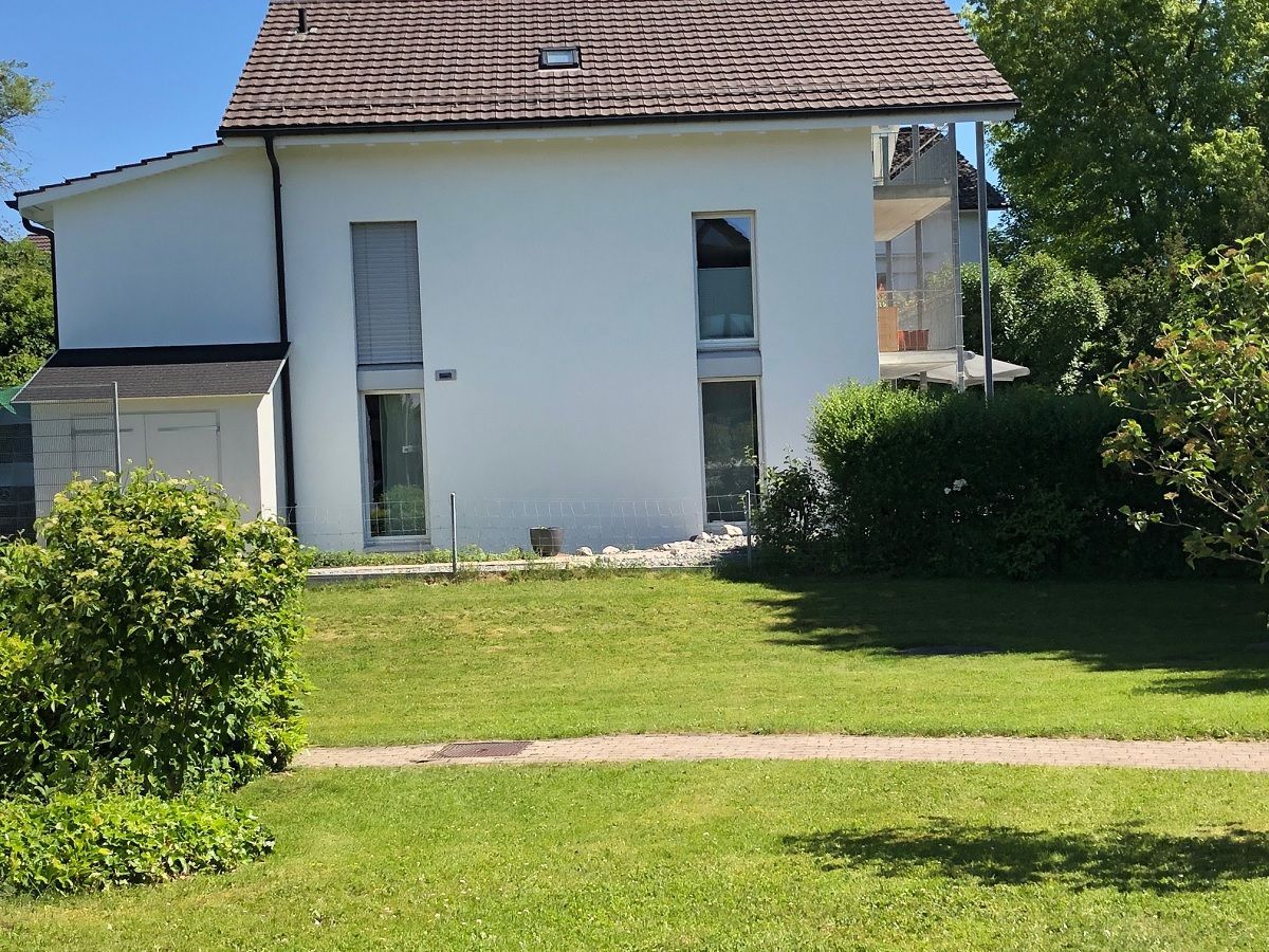 Ein weisses Haus mit Ziegeldach und einer grossen Wiese davor.