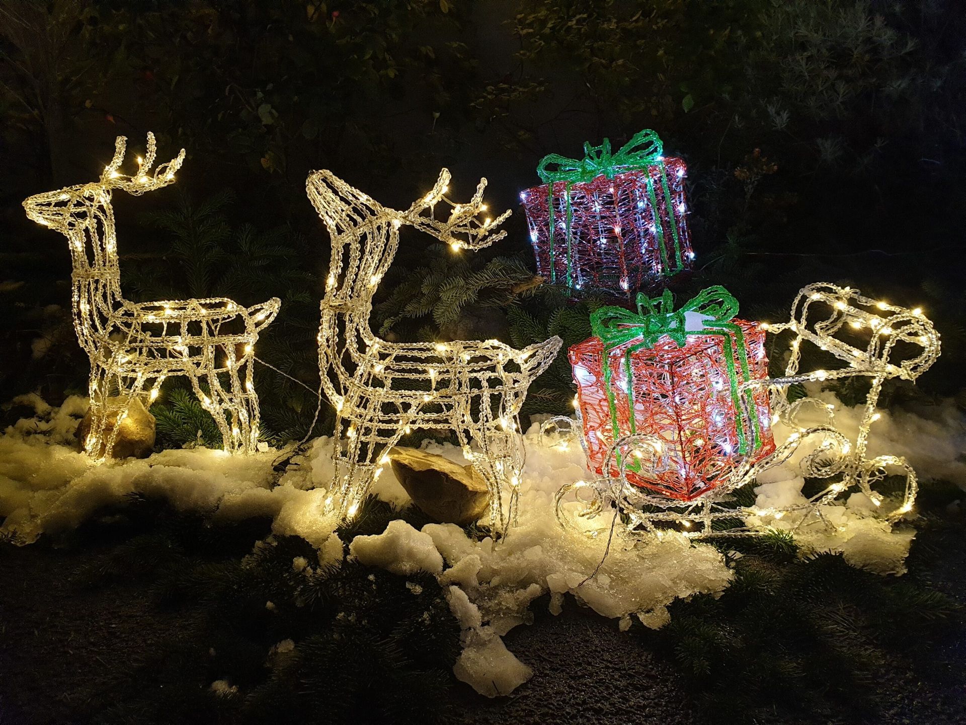 Eine Weihnachtsdekoration mit Rentieren und einem Schlitten mit Geschenken im Schnee.