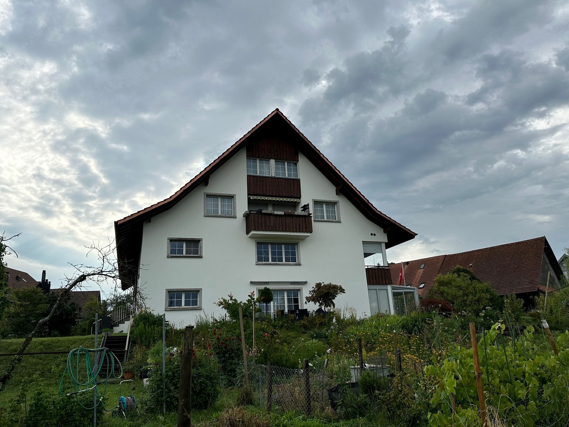 Ein grosses weisses Haus mit rotem Dach ist von Bäumen und Büschen umgeben.