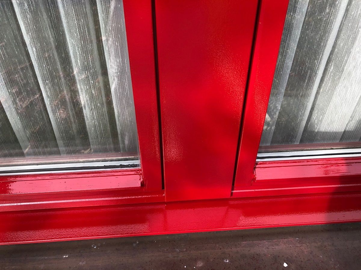 Eine Nahaufnahme eines roten Fensters mit weissen Vorhängen.