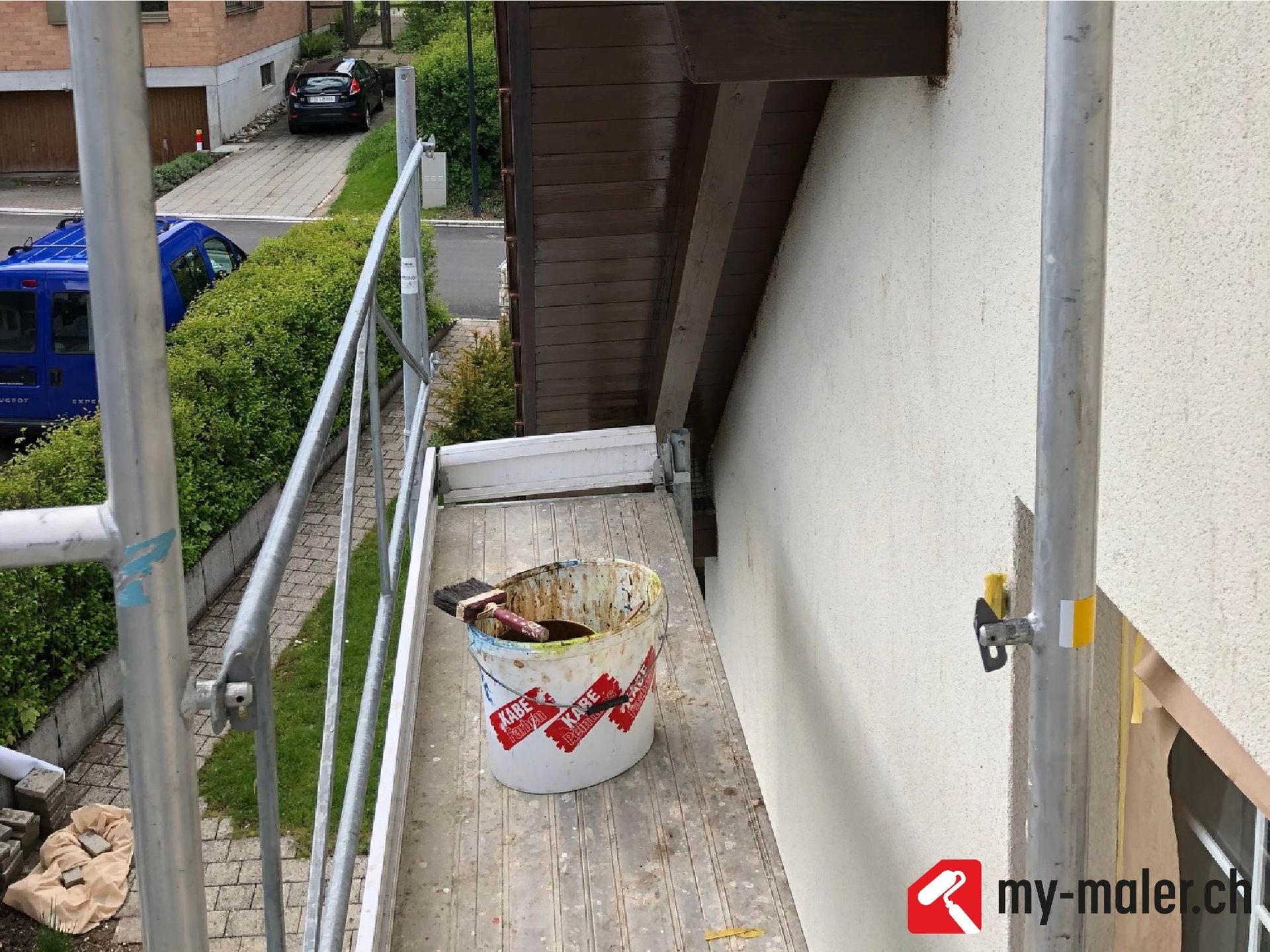 Ein Eimer Farbe steht auf einem Gerüst neben einem Gebäude.