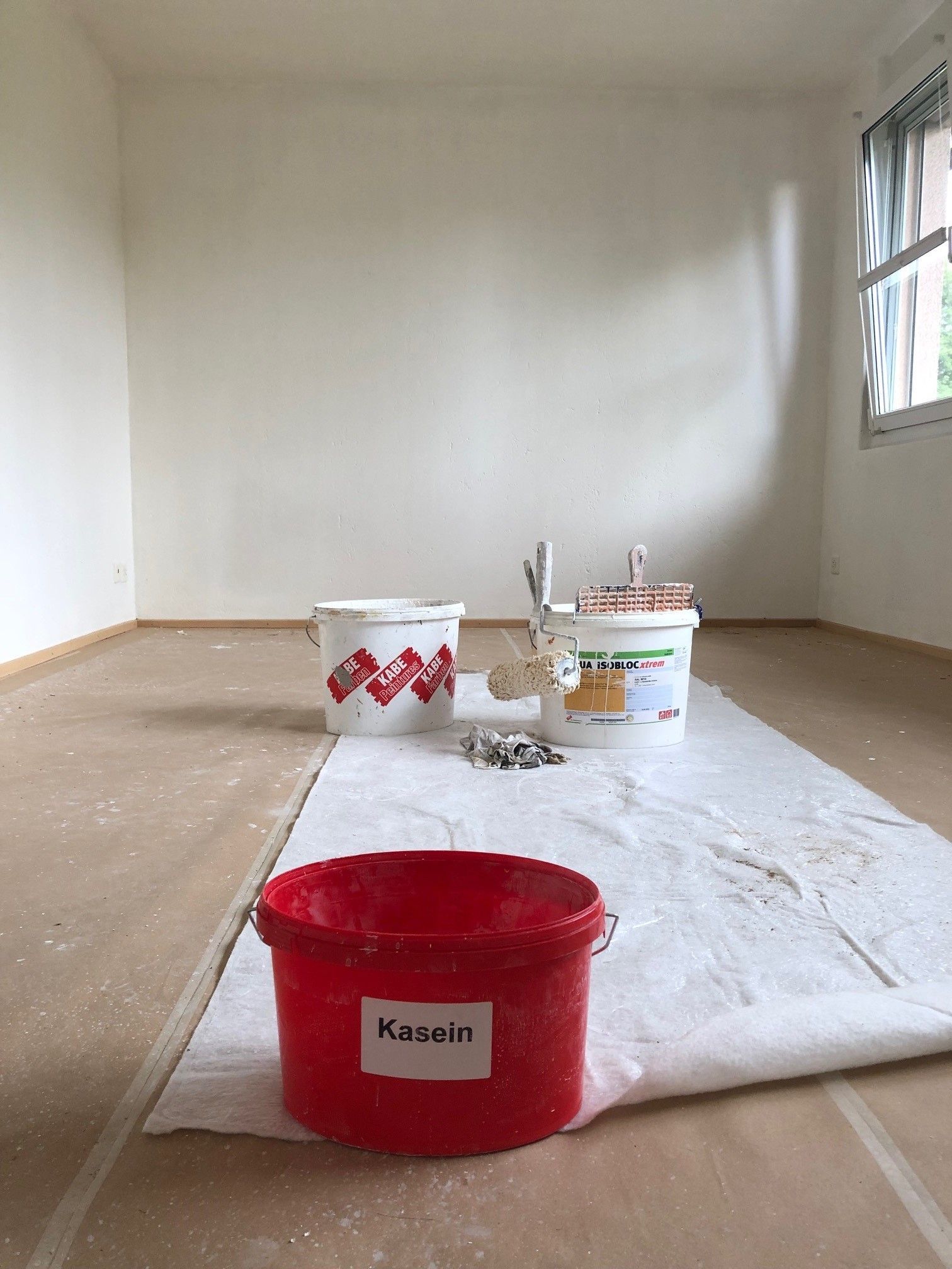 Ein Raum mit Farbeimern und Pinseln auf dem Boden.